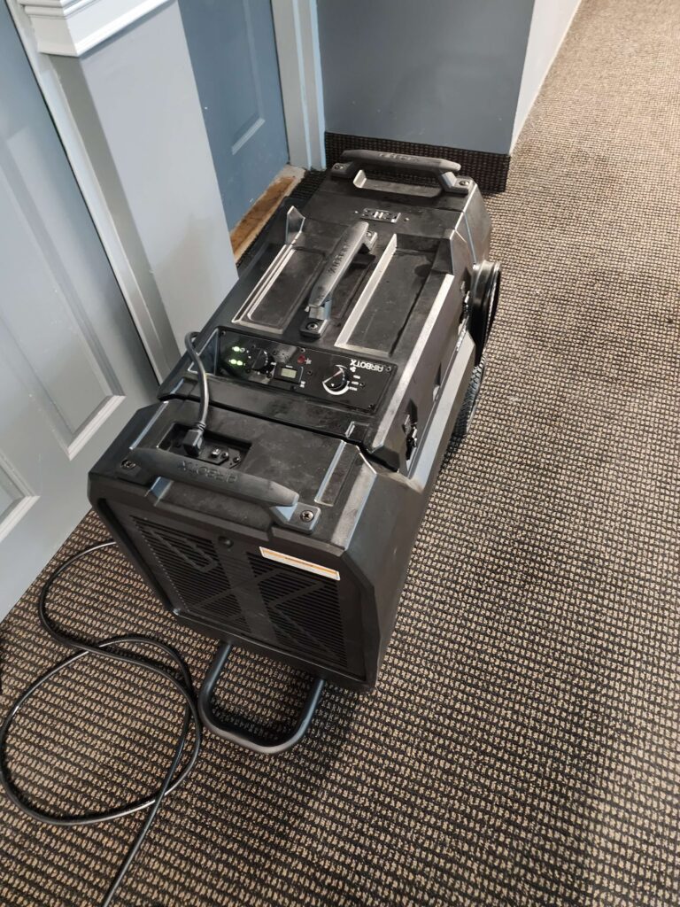 A black AIRBOTX industrial air mover with a control panel sits on a patterned carpet