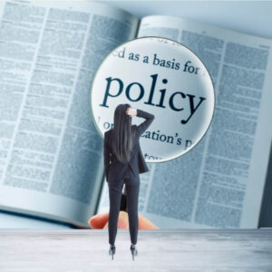 A person in a suit uses a magnifying glass to examine the word 'policy' in a