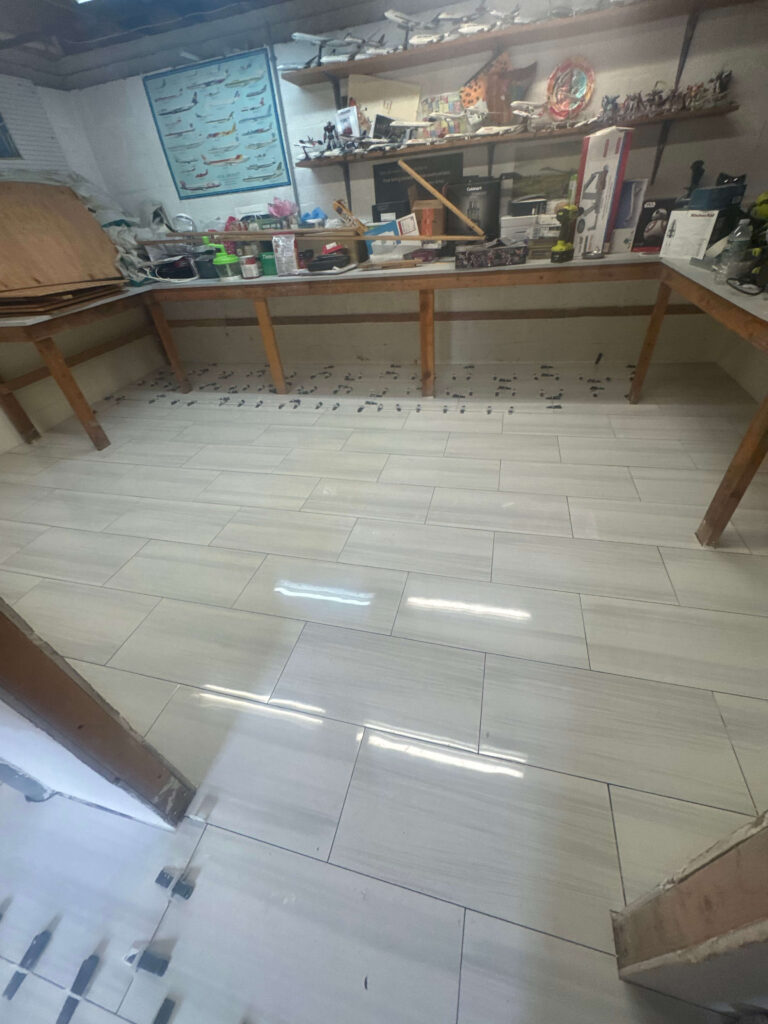 A hobby workshop features shelves of model airplanes, a long workbench, and newly installed light gray floor