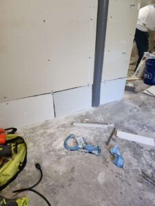 Drywall installation in progress with tools, dust, and a partially installed wall.