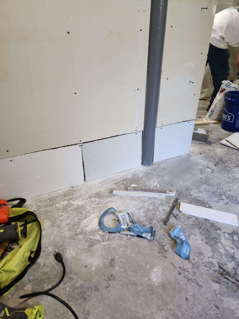 Drywall installation in progress with tools, dust, and a partially installed wall.