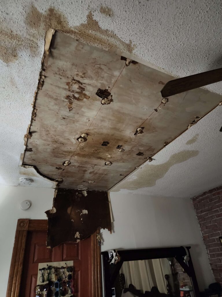 A ceiling shows severe water damage with a large, stained section detached and hanging. TITLE