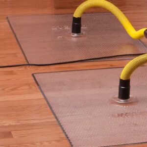 Clear floor drying mats with yellow hoses are suctioned to a wooden floor for water removal.