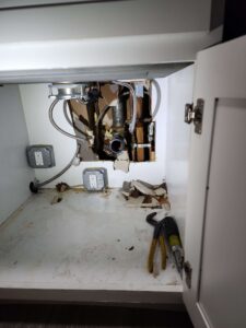 Under-sink cabinet with exposed plumbing, electrical outlets, water damage, and tools on the