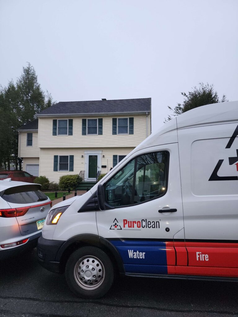 A white PuroClean service van, advertising water and fire restoration, is parked in front of a yellow suburban house