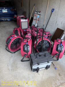 Pink PuroClean water damage restoration equipment, including fans and a dehumidifier, stored in a garage