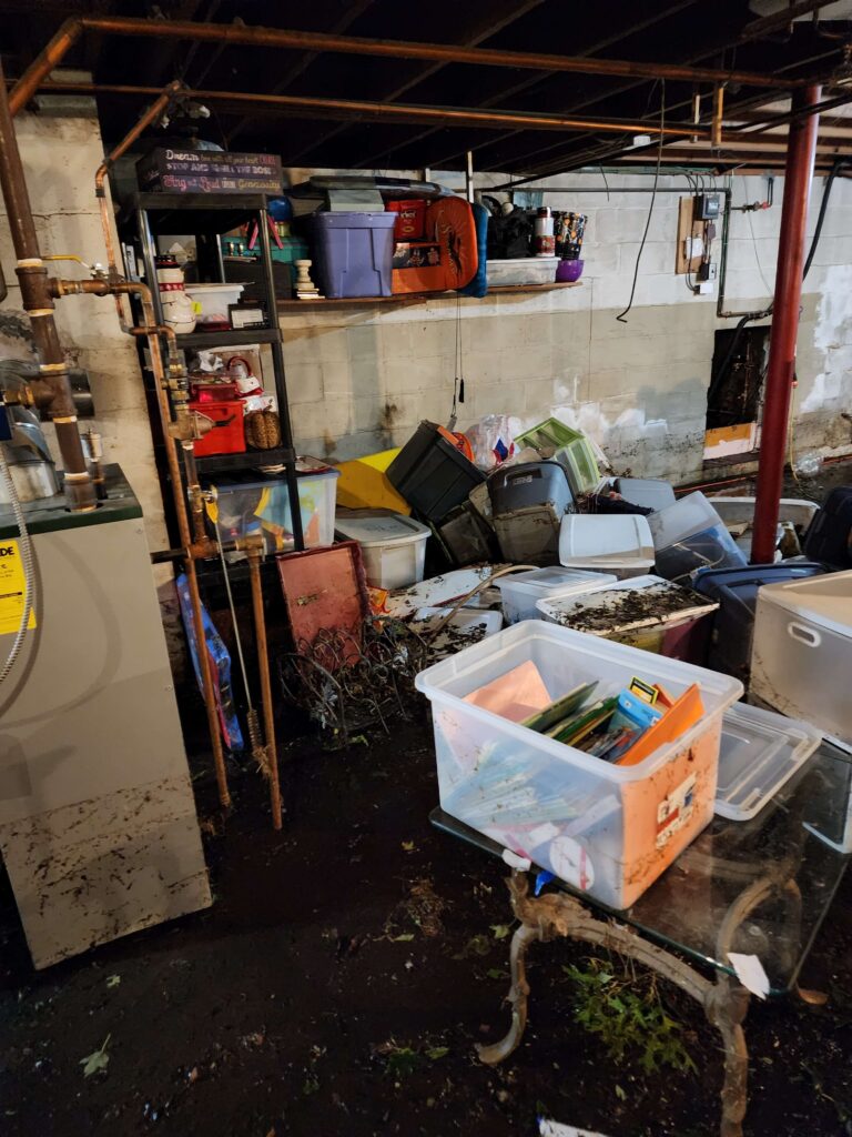 A cluttered, dark basement floor is covered in mud and debris with scattered storage bins.