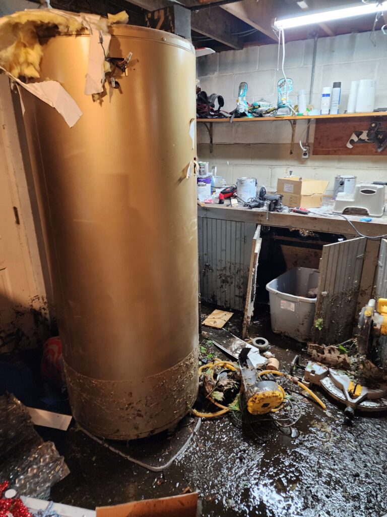 A large water heater stands in a severely flooded and debris-filled basement. TITLE