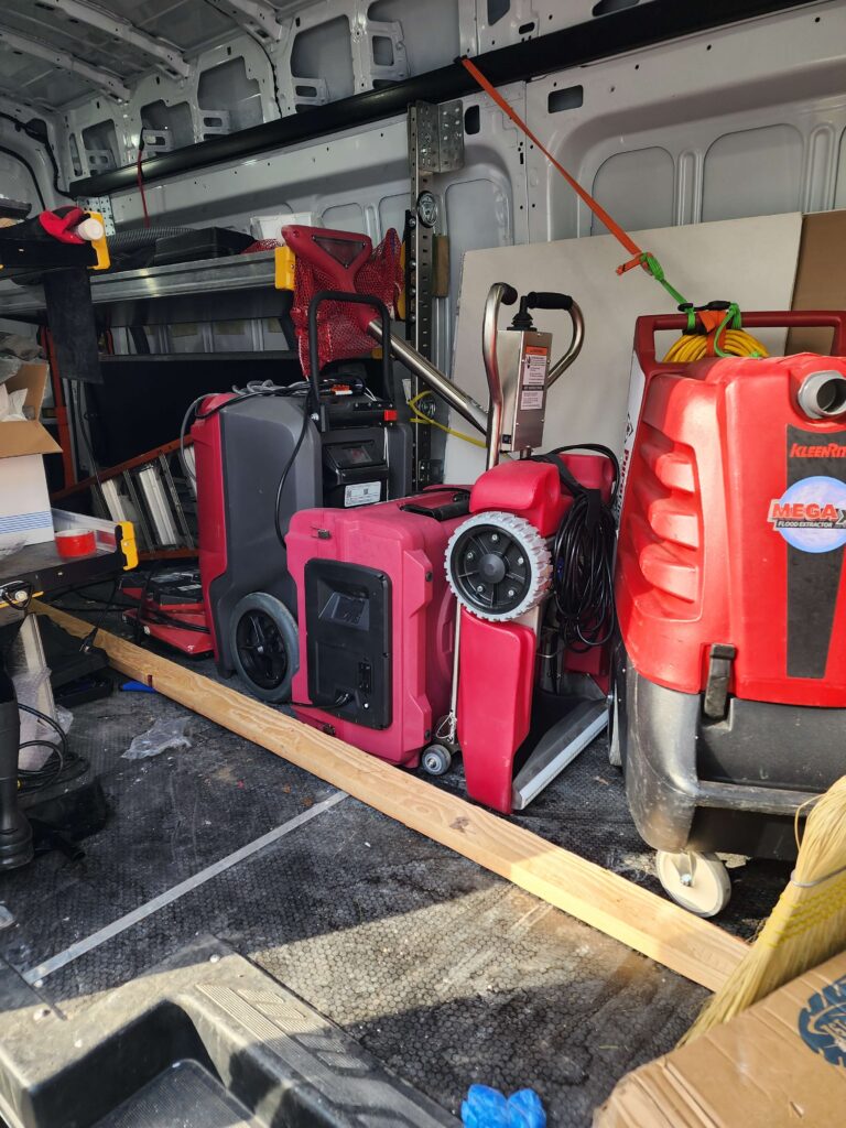 Interior of a work van showcasing red and black professional flood extraction and cleaning equipment. TITLE: