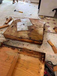 Water-damaged plywood and construction debris cover a concrete floor during a messy renovation. TITLE: