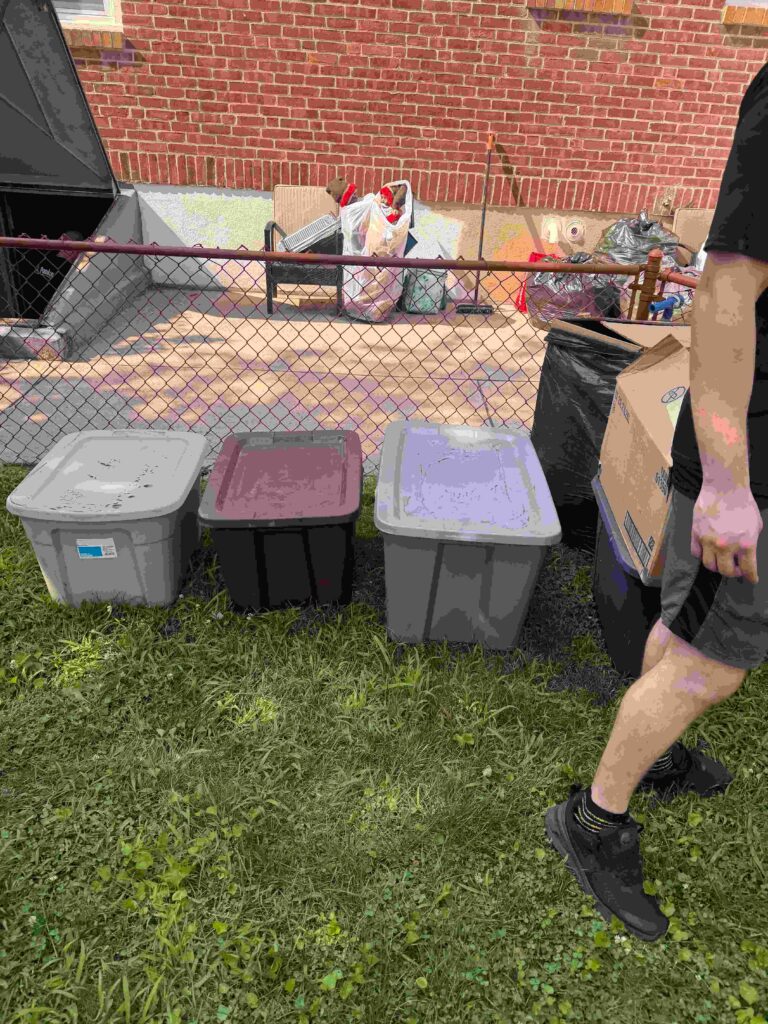 Three storage bins sit on green grass in front of a chain-link fence,