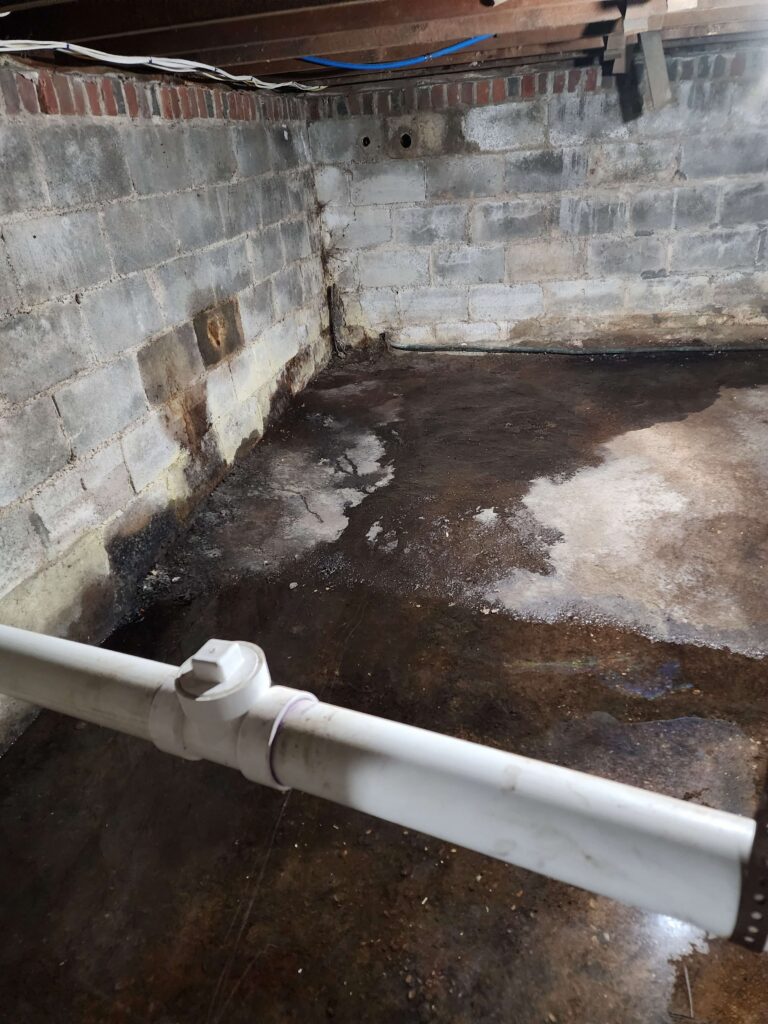 Damp concrete block basement corner with visible water stains, efflorescence, and puddles