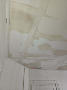 Extensive brown water stains and peeling paint cover a white ceiling and wall, indicating significant water damage.
