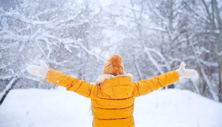 Pretty young girl wearing yellow jacket and knitted hat walking in snowy winter park.