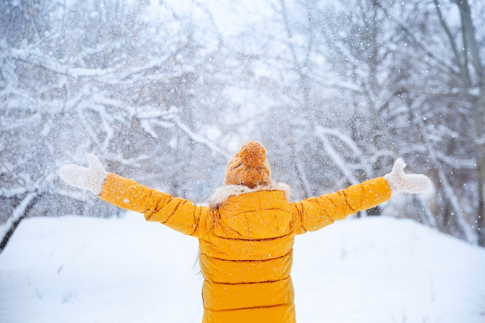 Pretty young girl wearing yellow jacket and knitted hat walking in snowy winter park.