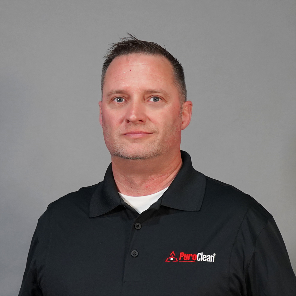 A man wearing a black PuroClean polo shirt looks directly at the camera.