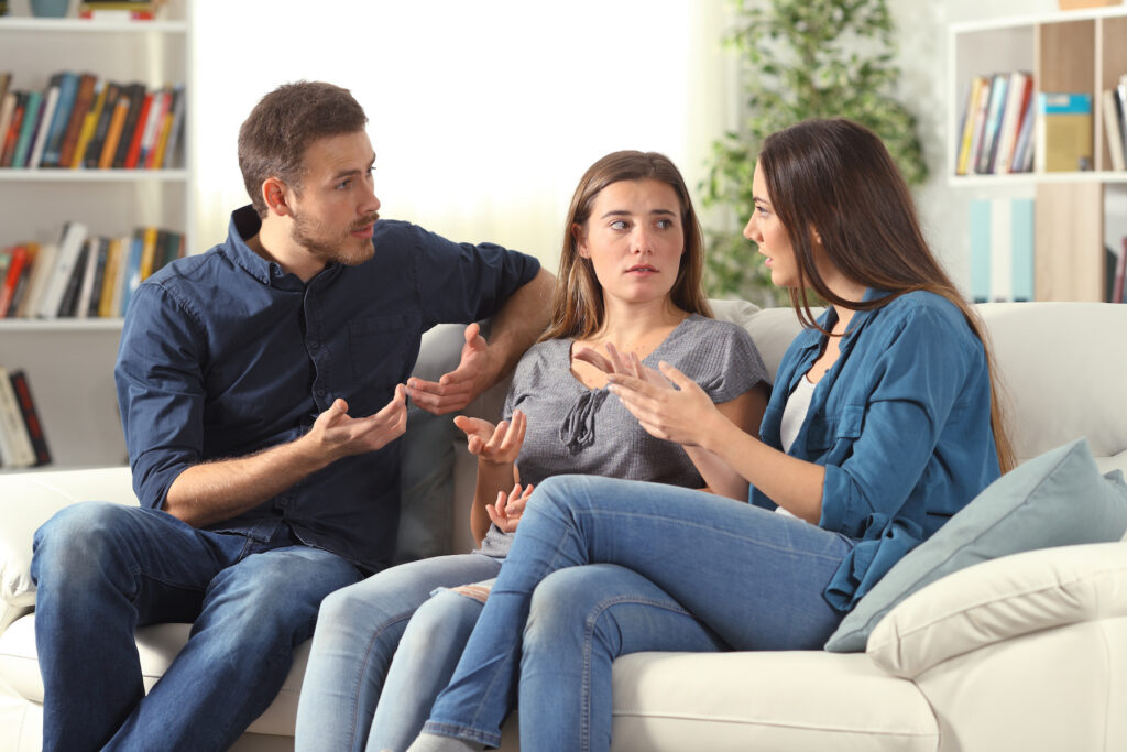 Three young adults engaged in a serious conversation while sitting on a couch in a cozy living room.