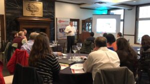 A speaker presents to an audience at a celebration event for Jim Bauer's 100th CE course with PuroClean Restoration Specialists.