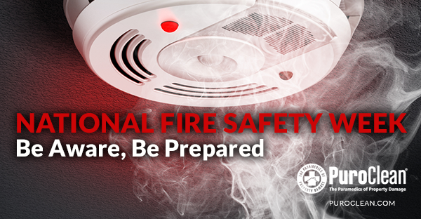 Smoke detector with a red light, surrounded by smoke, promoting National Fire Safety Week: Be Aware, Be Prepared.