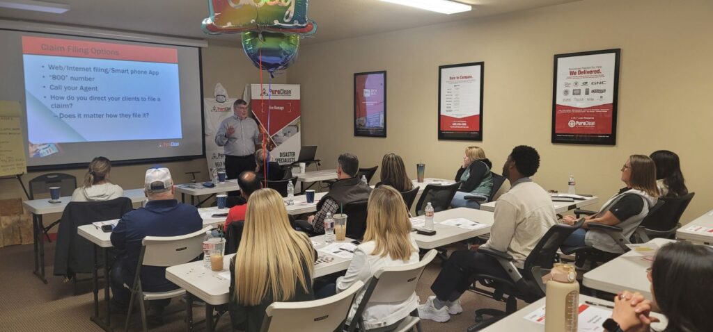 A classroom setting with a speaker presenting to a group of attentive insurance agents, focused on continued education.