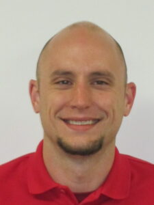 A smiling bald man with a goatee wears a red polo shirt against a white background.