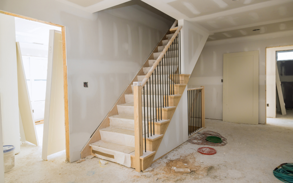 New home construction showing an unfinished wooden staircase, drywall walls, and concrete floor. TITLE