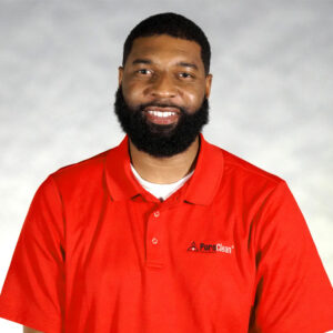 Smiling man with a beard wearing a red PureClean polo shirt against a light gray background.