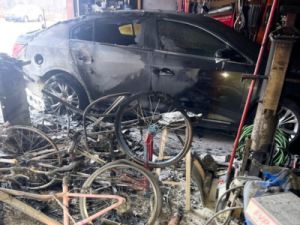 Garage fire damage restoration in Green Bay showing a burned car, scorched bicycles, and soot-covered interior after an intense vehicle fire.