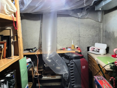 Drying equipment and containment setup in a Green Bay basement during residential basement water damage restoration, with shelving and storage items visible.