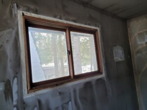 Heavy black soot staining on a room's walls and ceiling surrounding a wooden window frame after a house fire.