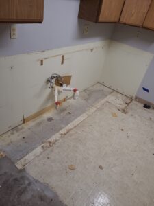 Exposed plumbing and extensive floor water damage in a commercial or home kitchen under renovation.