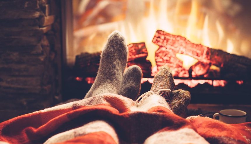 Two people warming their feet by the fire while practicing fall fire safety