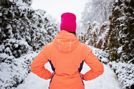 Woman in orange jacket stands on a snowy path with her back to the camera