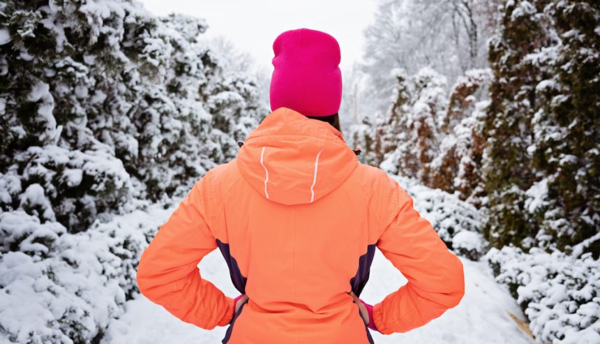 Woman in orange jacket stands on a snowy path with her back to the camera