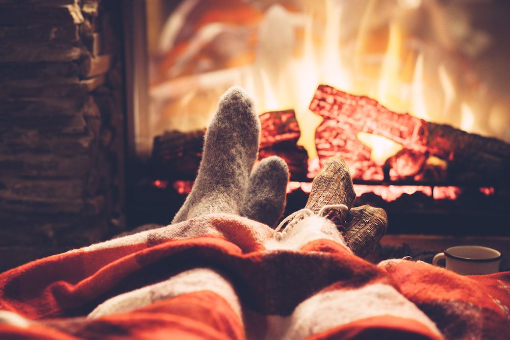Two people warming their feet by the fire while practicing fall fire safety