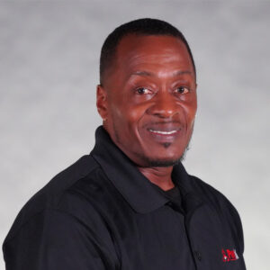 Smiling man in a black polo shirt against a gray background, representing the team on the "About Us" page.