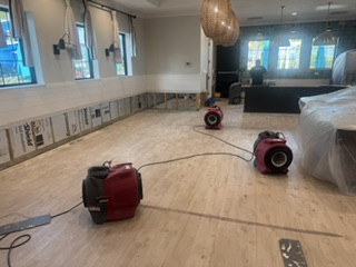 Water damage restoration in a large room with exposed walls and three industrial drying machines. TITLE: