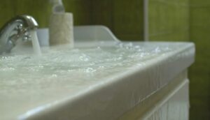 Water gushes from a faucet, overflowing a bathroom sink and spilling onto the vanity.