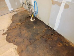 Severe water damage on a subfloor with exposed plumbing and a partially finished wall.