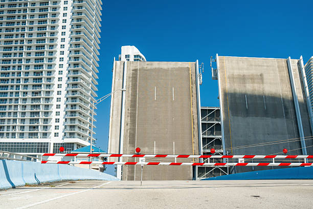 Traffic barriers block a raised drawbridge next to a modern high-rise building under a clear blue sky.