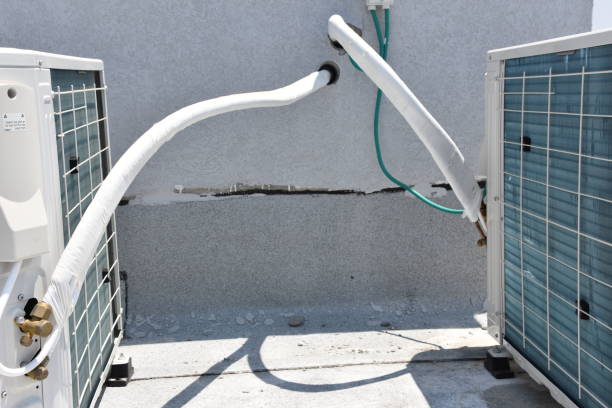 Two outdoor air conditioning units are connected by insulated white pipes and green lines on a concrete surface