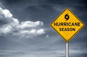 A yellow diamond warning sign for 'HURRICANE SEASON' stands against a dark, cloudy