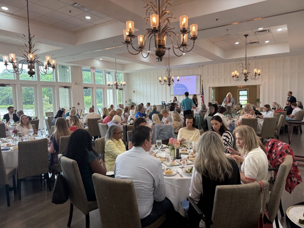 Guests socialize and dine at a business luncheon in a bright event room with large windows and