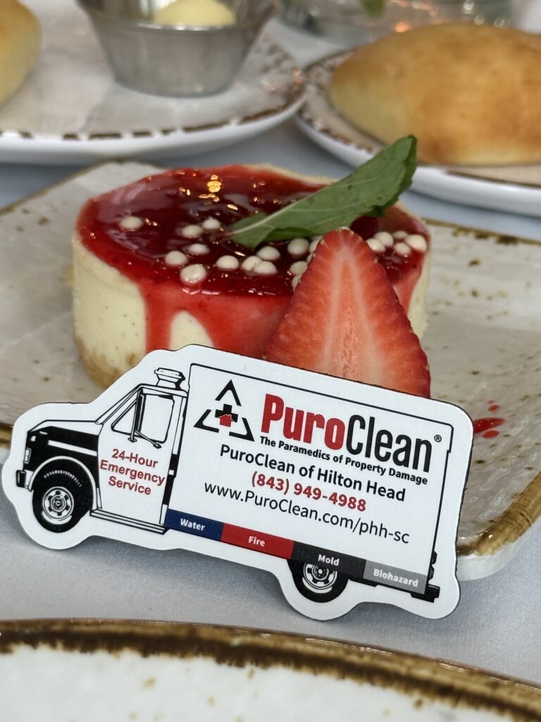 A truck-shaped PuroClean business card rests in front of a strawberry cheesecake with