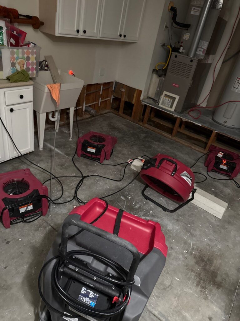 Red drying fans and a dehumidifier are set up in a utility room with exposed wall studs for