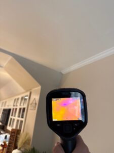 hidden damage A hand holds a thermal camera displaying heat variations on an indoor ceiling.