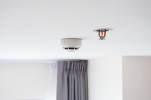 Ceiling‑mounted fire sprinklers and smoke detector providing home fire protection and early suppression.