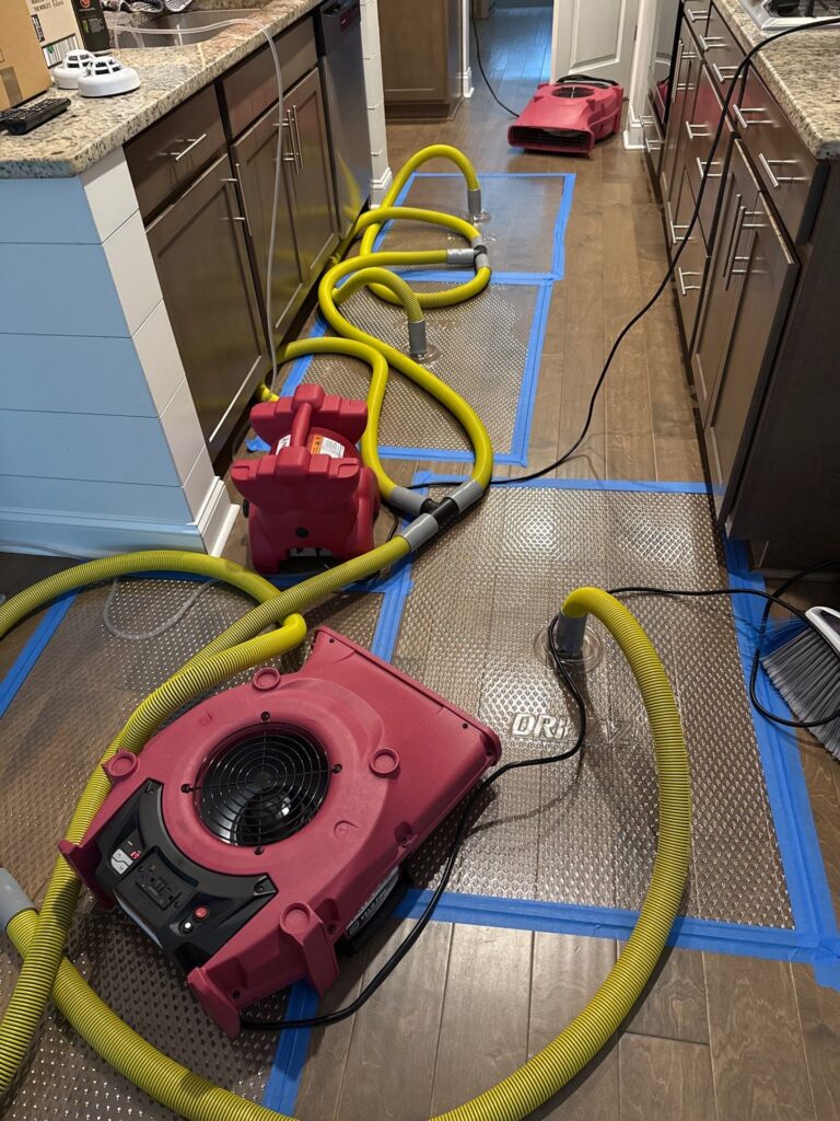 Water damage restoration equipment, including red air movers and yellow hoses, dries a kitchen's hardwood