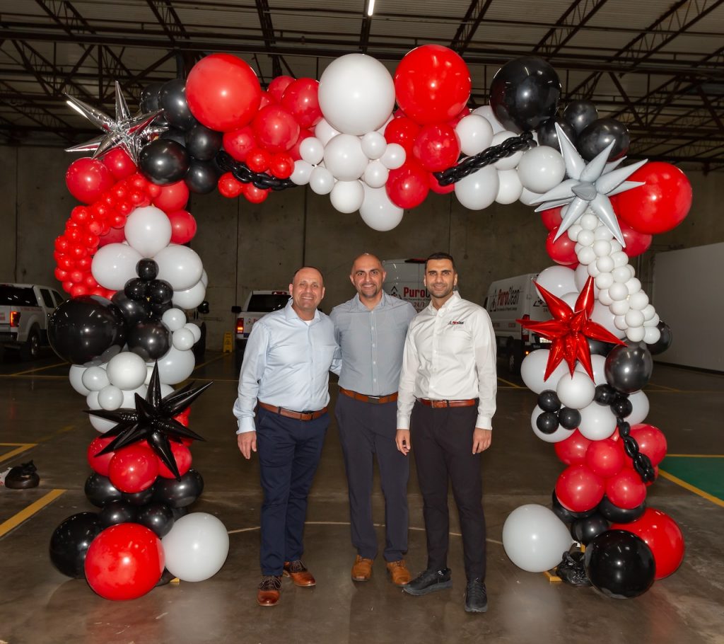 PuroClean team members pose in front of an archway of balloons.