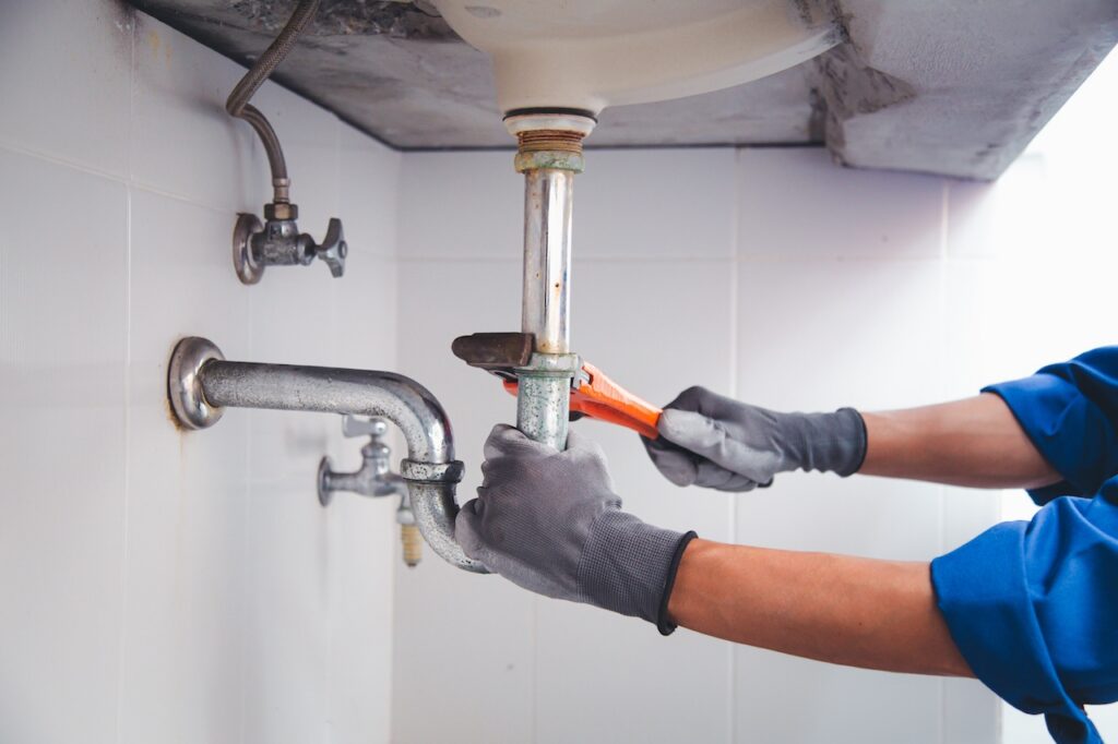 Plumber testing and repairing a leaking pipe after an underground water leak. Technician plumber using a wrench to repair a water pipe under the sink. Concept of maintenance, fix water plumbing leaks, replace the kitchen sink drain, cleaning clogged pipes is dirty or rusty.